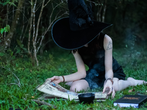 Woman with witch hat sitting in grass reading book