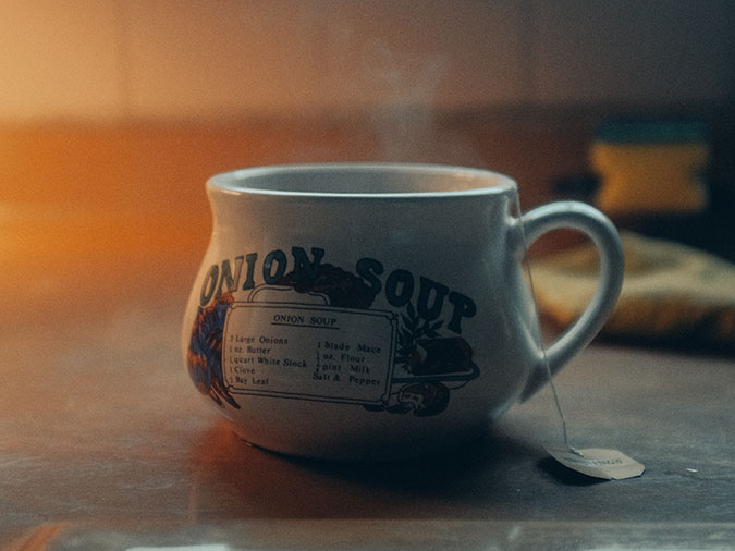 Delicious steaming onion soup for the soul in a ceramic mug that says "Onion Soup" and has a cute little painting on it with the ingredients...of which The Onion is one.