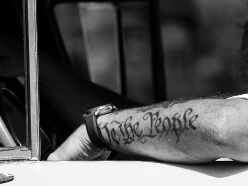 Man's arm over the driver's side window with tattoo We The People