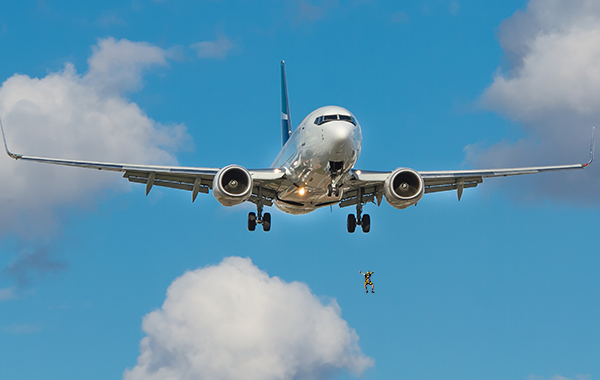 Plane in the sky and clouds with a person pictured jumping below the plane